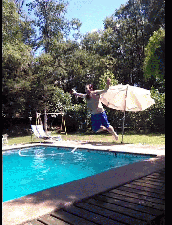 man jumping in water next to umbrella with board