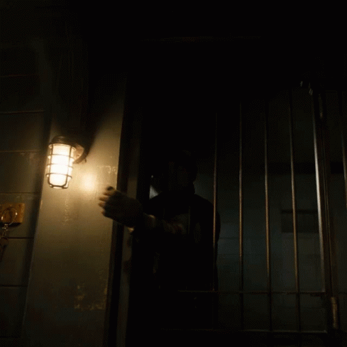 a man in a dark room is reaching into the  cell door