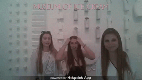 three women stand next to a wall with an ice cream advertit