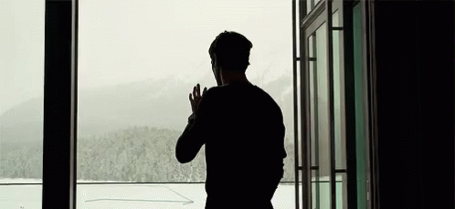 the silhouette of a man in a black shirt is looking out an airport door at snow covered mountains