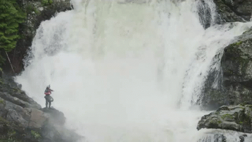 the person stands near a waterfall and looks up at it