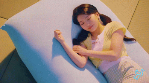 young asian woman laying on a pink pillow while using her cell phone