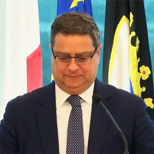 man with black jacket and tie sitting in front of flags