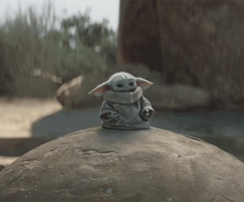 the baby yoda doll is sitting on top of a rock