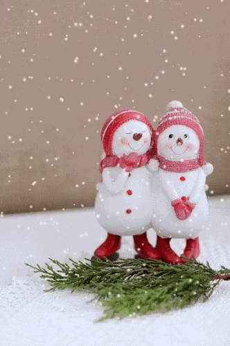 two snowmen standing next to each other on top of a pile of snow