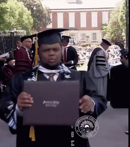 a boy dressed in graduation garb holds up a laptop
