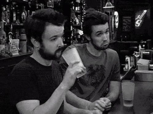 two men at the bar one drinking while another looks angry