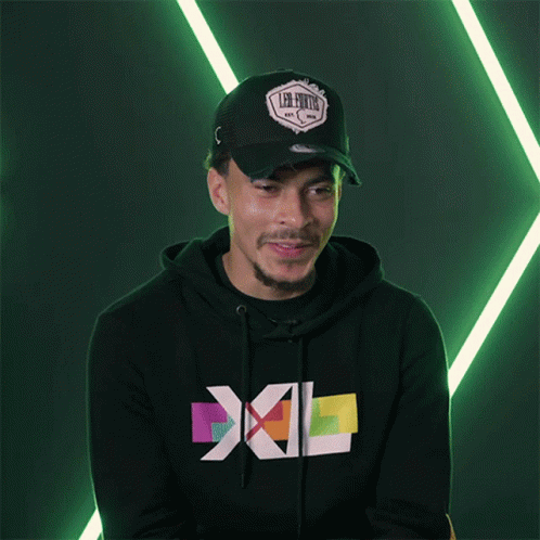 a man with black hoodie and cap next to a green wall