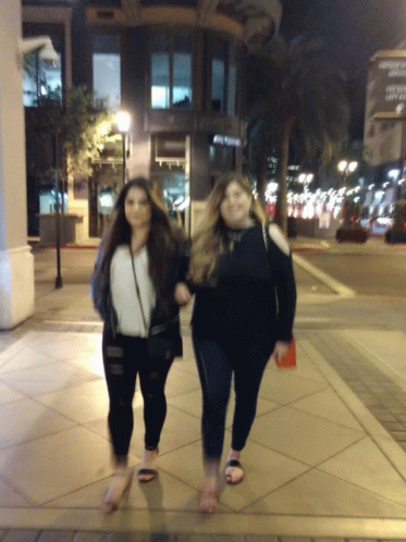 two women with long hair walking down a sidewalk at night