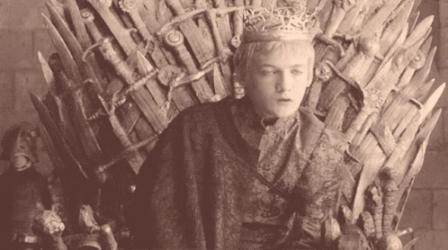 a woman sitting on the iron throne, wearing a tiara