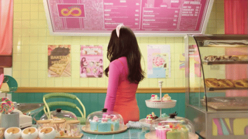 a woman standing at a counter with cakes and other items