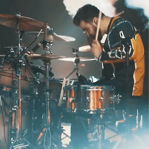 drummer playing the drums on stage, while smoke billows behind him