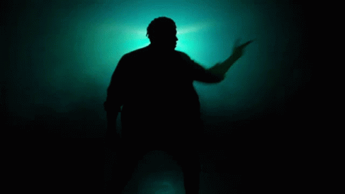 a man in the shadows of dark holding up a lit object