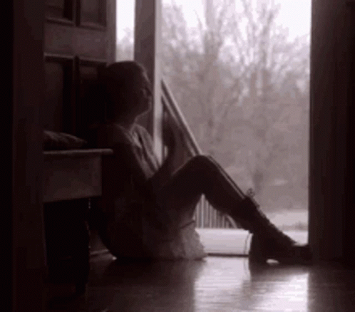 a person sits on the floor by a window