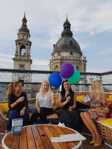 four women sitting on blue chairs with colorful balloons