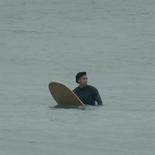 the man is sitting in the water with his surfboard