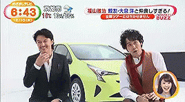 two asian men sitting down next to a car