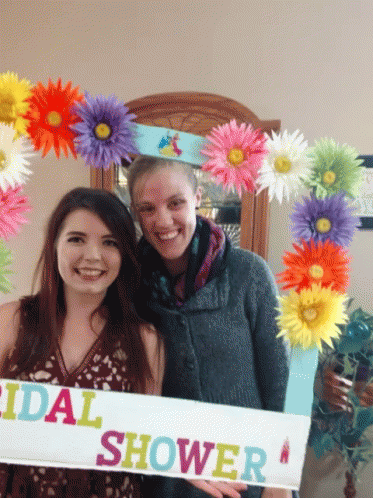 two women holding up a large sign surrounded by multi - colored flowers