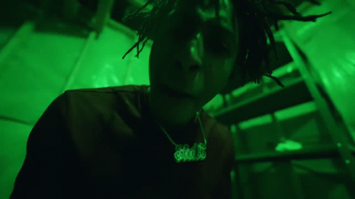 a man with dreadlocks on his head stands against green lighting