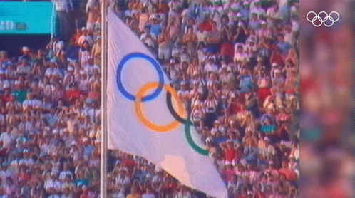 an olympic flag flying in the middle of a large crowd