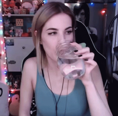 a woman is holding a glass of water to her mouth