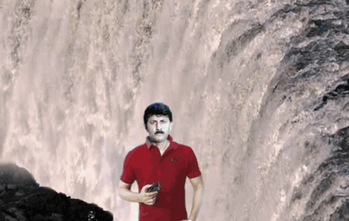 a man in blue shirt standing near a waterfall