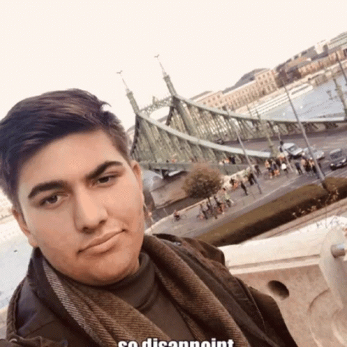 a man looking at the camera in front of a bridge