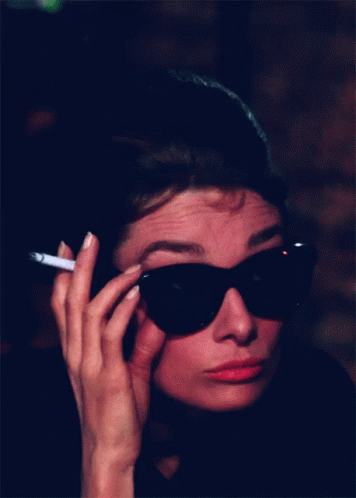 a woman wearing sunglasses, smoking a cigarette