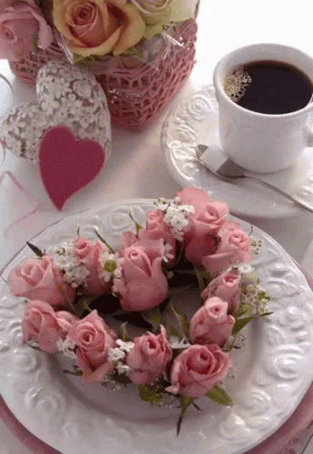 a heart shaped arrangement of flowers sits next to a coffee cup