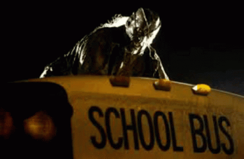 a man standing behind a school bus at night
