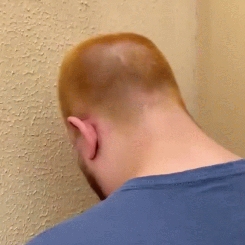 the head of a man with a shaved head standing against a blue wall