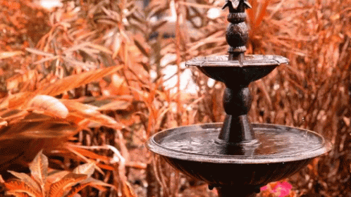 a tall fountain sitting in front of blue bushes