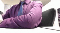 a man in a purple shirt and necktie is sitting at his desk