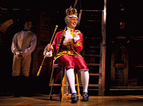 actors sitting on stage in costumes performing on a stool