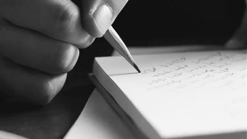 a person sitting at a table writing with a pen