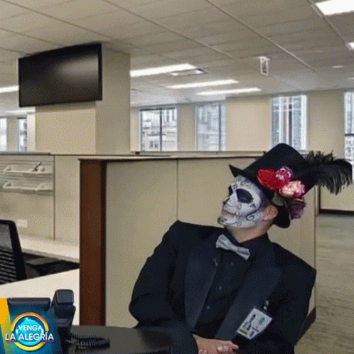 a skeleton wearing a tuxedo sits on a cubicle