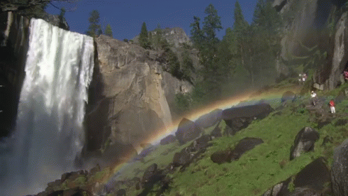 a rainbow is on the waterfall while people walk by