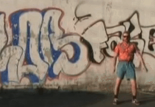 a man is walking in front of a wall that has been sprayed with graffiti