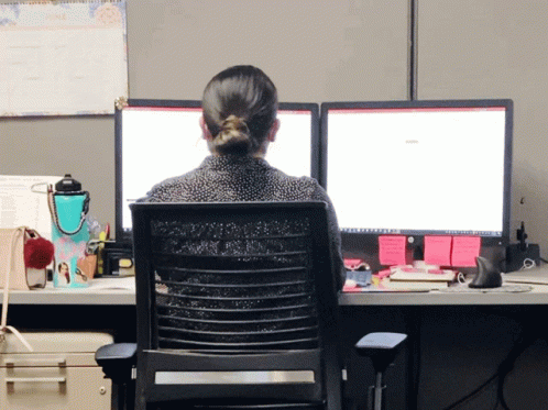 a woman sitting at a desk with two computer screens