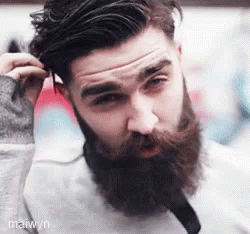 a bearded man holding up his hair and smoking a cigarette