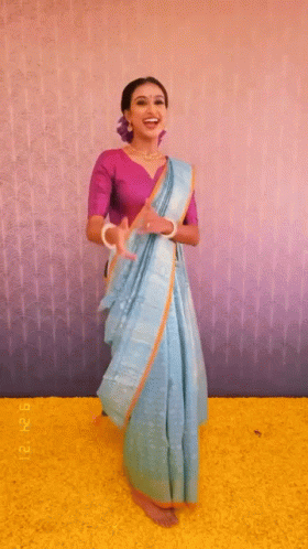 a woman dressed in a saree standing and smiling