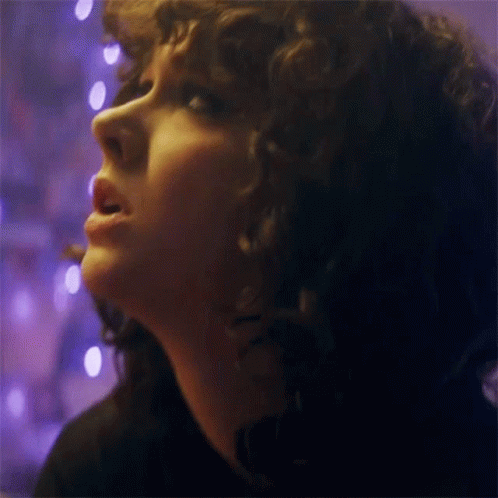 the young woman with the large curls stares at the pink lights