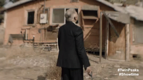 the man is wearing a suit standing in front of a shack