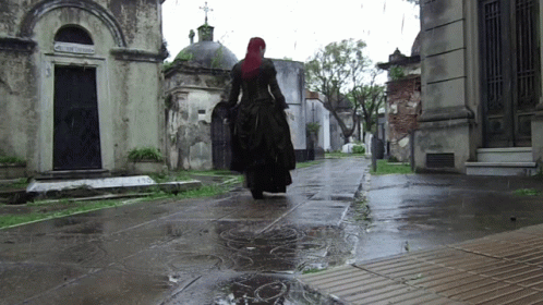 a woman walking along an empty cemetery in the rain