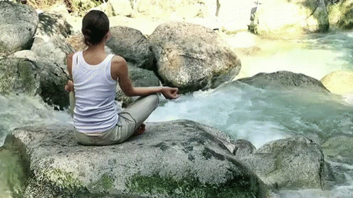 the woman is sitting on a rock in front of some water