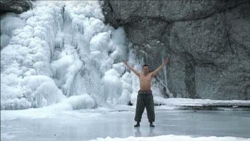 a man standing on frozen water in front of a waterfall