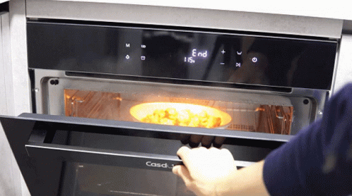 someone wearing gloves puts food in an oven