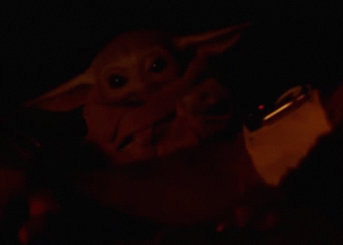 a child yoda doll holding a cell phone in the dark