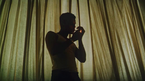a man in silhouette using a cellphone while standing behind curtains