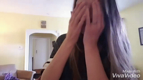 a girl is standing in the middle of a room, her hands covering her face